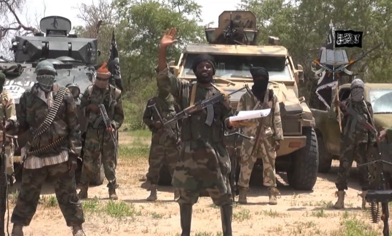 Boko Haram terrorists dressed in military camouflage huddling assault rifles and standing in front of some trucks