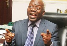 Falana in a grey suit, with fingers raised
